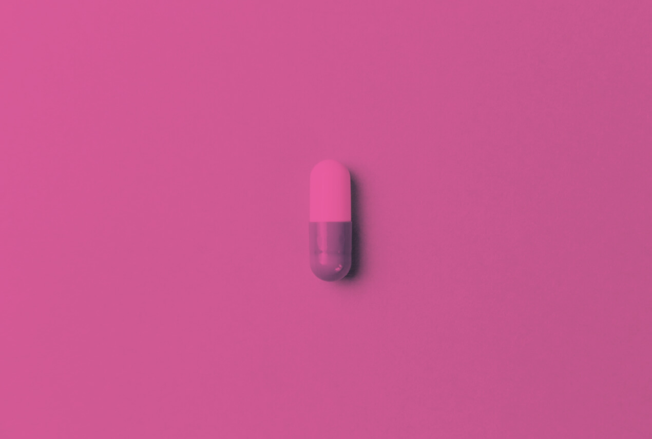 A pill sits alone on a table and a pink filter covers the whole image.