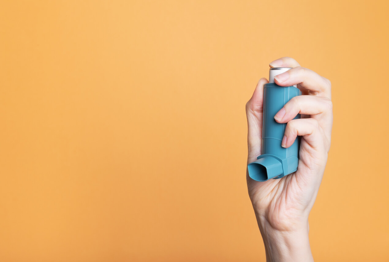 A hand holds up a teal inhaler against an orange background.