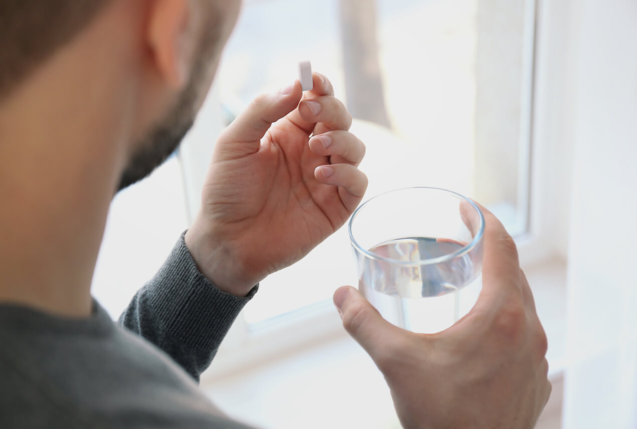 A man holds a diuretic pill in his left hand and a glass of water in his right hand.