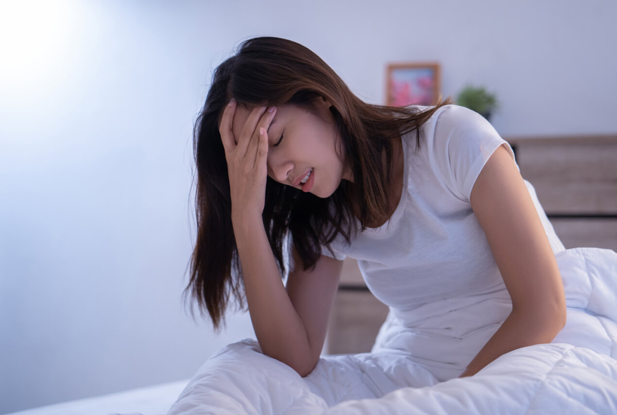 A woman sits in bed with her head in her hand.