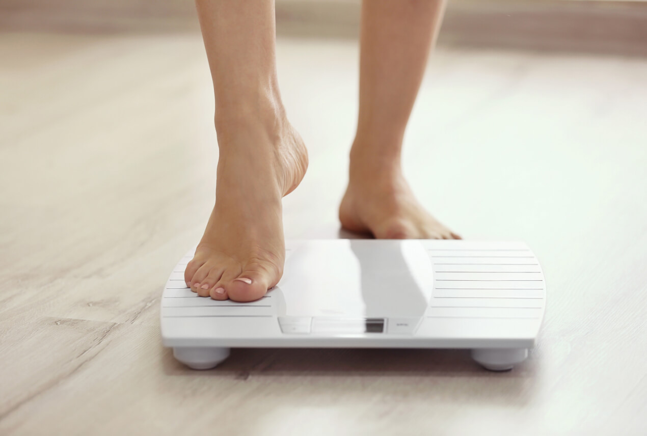 A foot steps onto a white scale on a wooden floor.