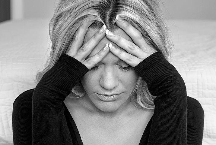 A black and white photo shows a distressed woman wither her forehead in her hands.