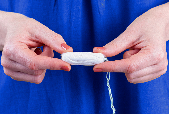 A person holds a tampon in two hands with their fingers.