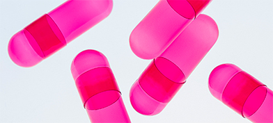 Pink, translucent pill capsules are scattered on a white background.