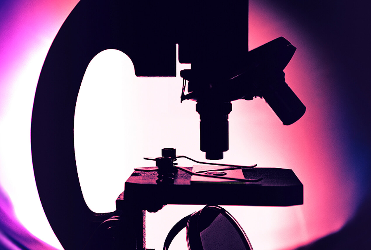A microscope is lit from behind by a pink and purple light