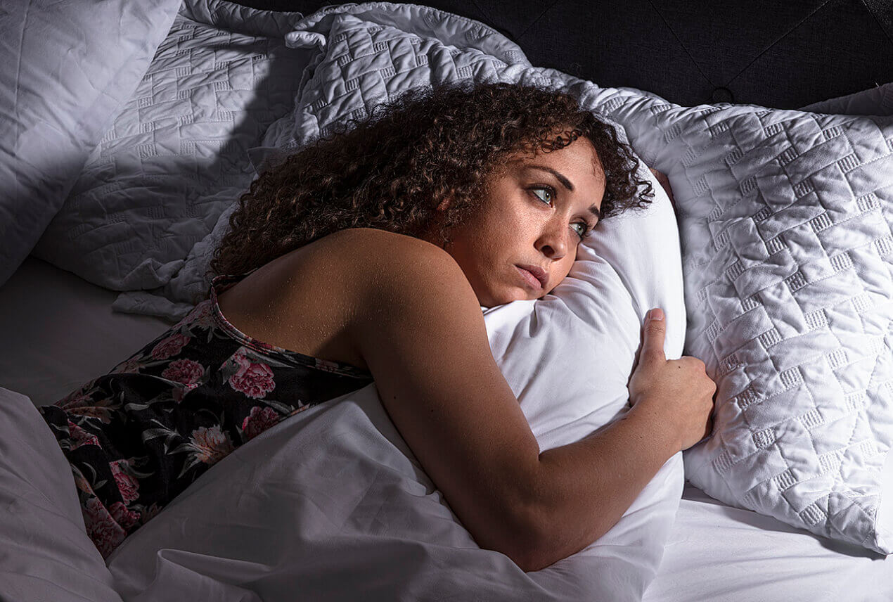 A woman lays in bed hugging her pillow trying to sleep.