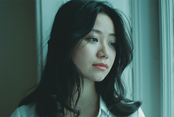 A green-ish filter covers an image of a woman looking out a window.