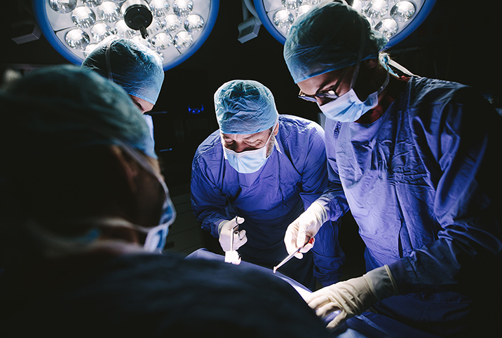 A team of surgeons and doctors lean over a person as surgery is performed on them.