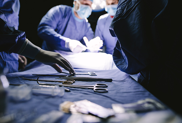 Doctors in medical gear crowd around a tray with surgical instruments on it.