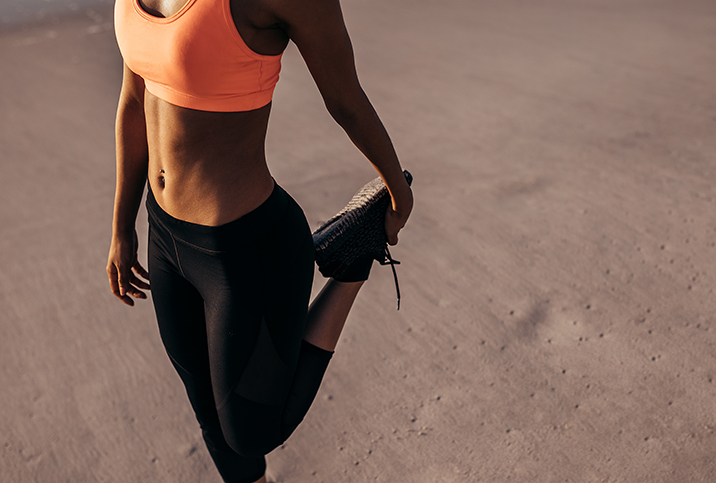 A woman dressed in activewear stretches her leg.