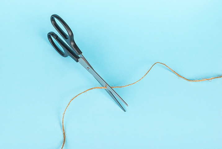 A pair of scissors cuts a string of twine against a blue surface.