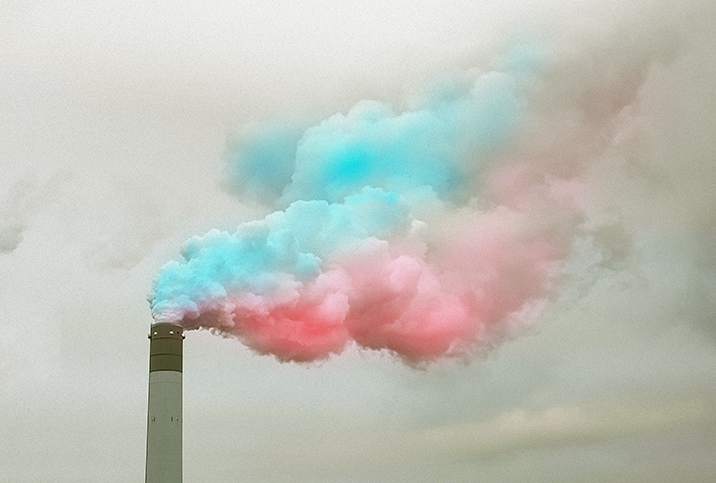 Blue and pink smoke billows out the top of a smoke stack. 