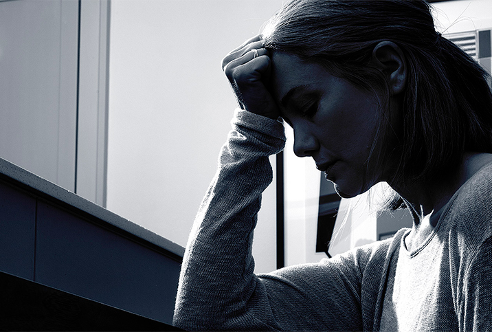 A black and white photo shows the profile of a person with their head in their hand.