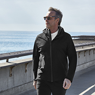 A man in activewear and sunglasses walks along a body of water in the sun.
