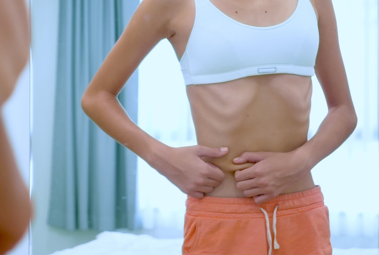 A very thin woman pinches her skin along her abdomen.