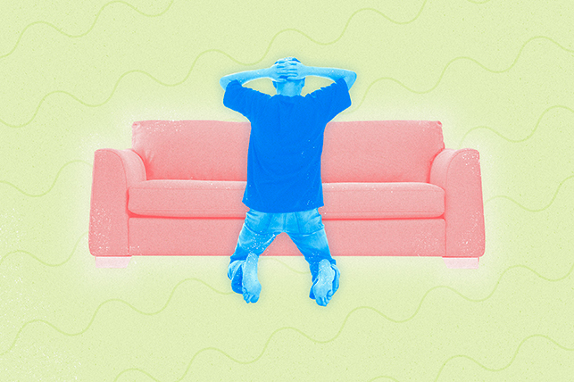 A blue man kneels in front of a couch with his arms behind his head.
