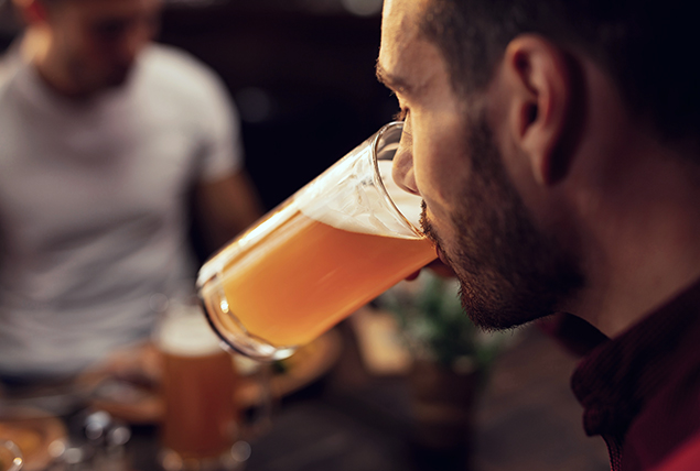 A man is drinking a glass of beer at a restaurant.