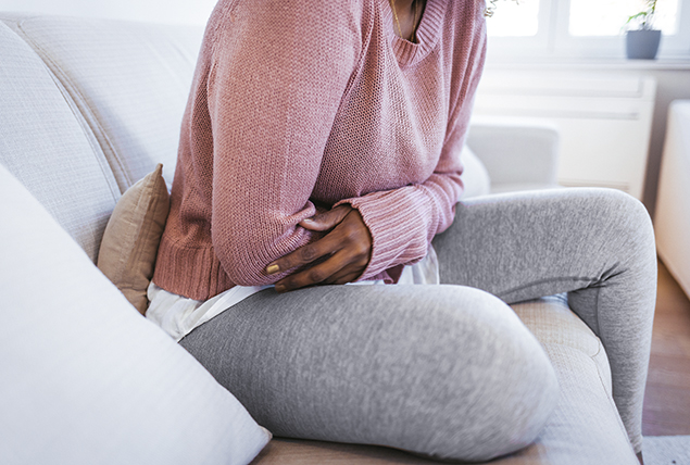 A woman holds her stomach while sitting on the sofa.