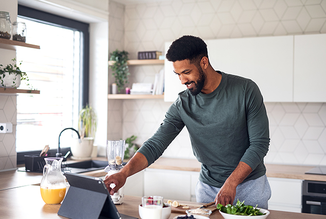 A man smiles as he touches his tablet on a kitchen counter while cooking.