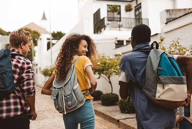 A teenage girl walks to school with two teenage boys.