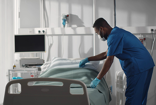 A man in blue scrubs makes a hospital bed.