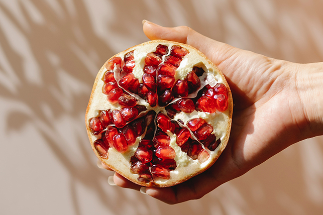 A hand holds half of a pomegranate with the seeds showing.