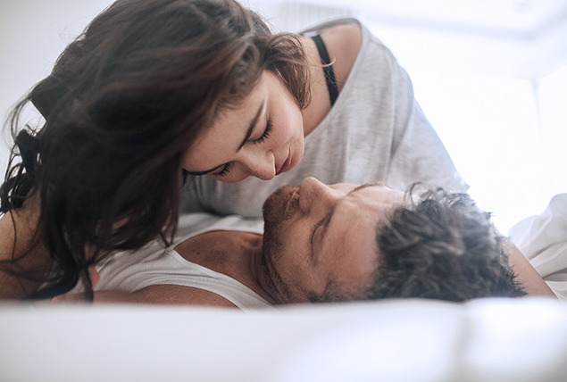 A woman lays over a man leaning in for a kiss.