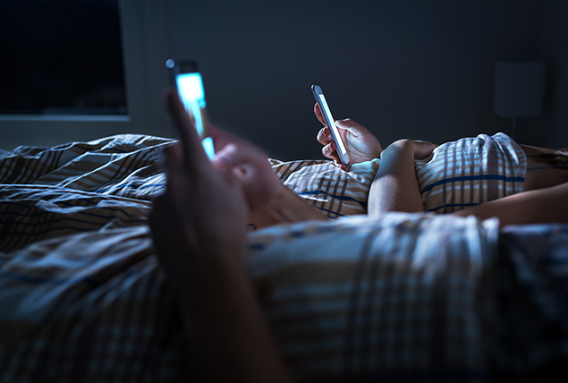 A couple lays in bed at night looking at social media on their cellphones.