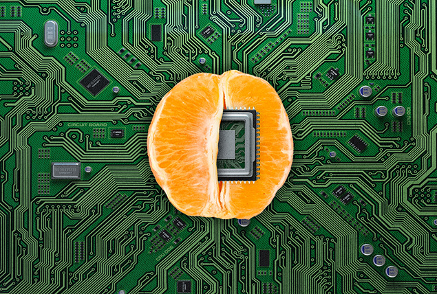 Half of an orange sits on a motherboard with a computer chip inside of it.
