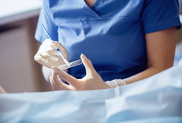 A nurse holds a clear microscope slide as she tests for cervical cancer.