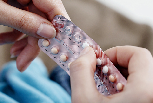 A pair of hands hold a packet of birth control pills.