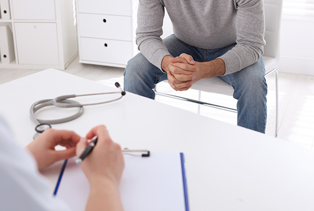 A man sits on a chair while listening to a doctor. 