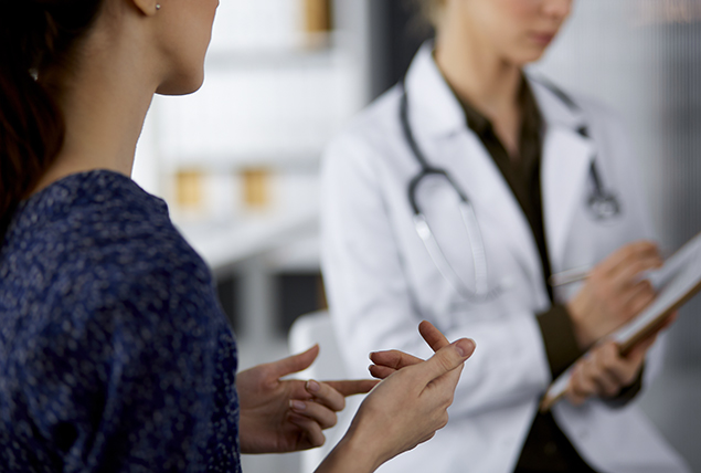 A woman talks to a doctor as they write on a clipboard.