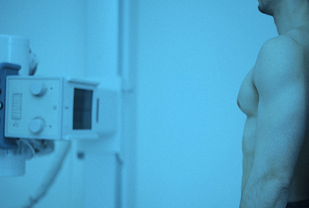 A shirtless man stands in front of a machine to detect breast cancer cells.