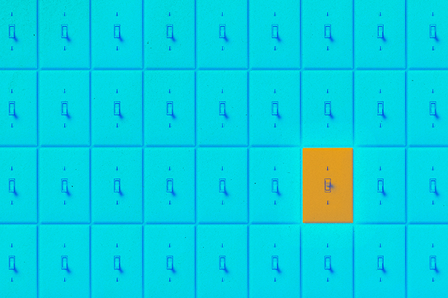 A yellow light switch is in the ON position along a wall of teal light switches in the OFF position.