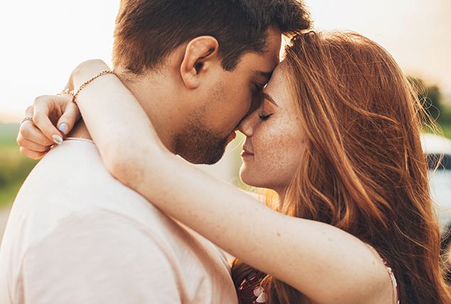 A woman holds a man by embracing him around his neck with their foreheads pressed together.