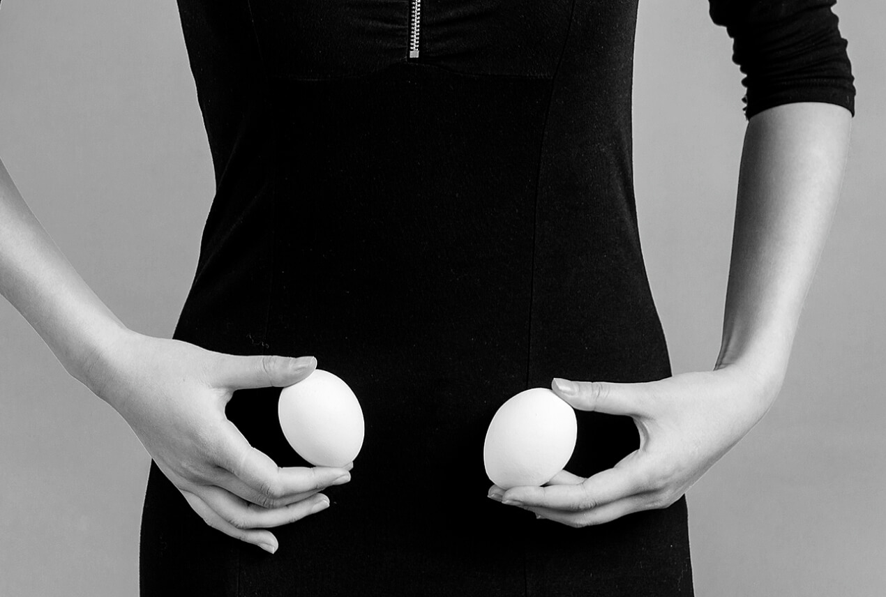 A woman holds an egg in each hand over her ovaries.