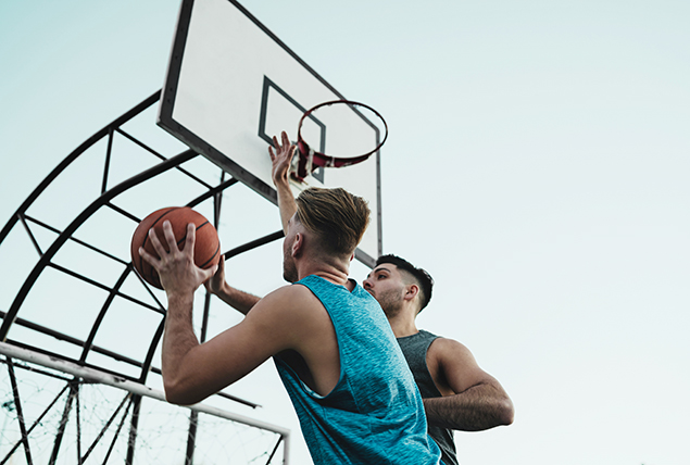 Two men are playing basketball outside.