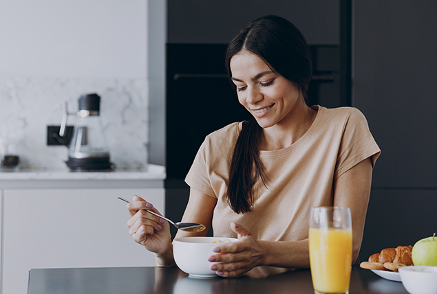 A woman sits down at a kitchen counter eating a fiber-rich breakfast.