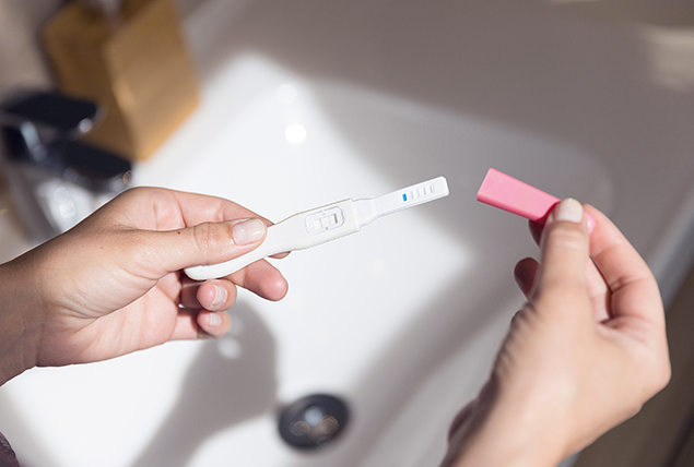 A pregnancy test is held over a sink in the sunlight.