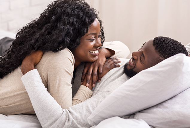 A woman leans onto a man while they lay down in bed.