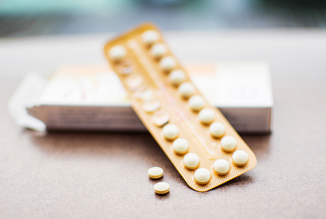 A packet of birth control pills lays against an open box with two pills sitting next to it.