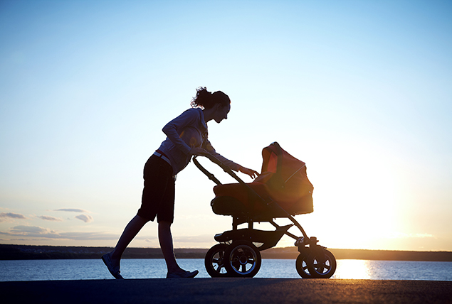 A woman walks her baby in a stroller against the sunset.