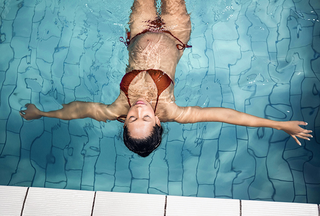 A pregnant woman in a red bathing suit floats on her back in a swimming pool.