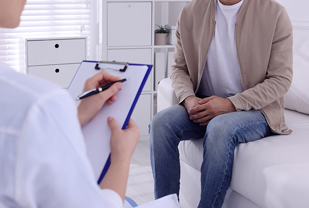 A man sits on a couch across from a doctor with a clipboard.