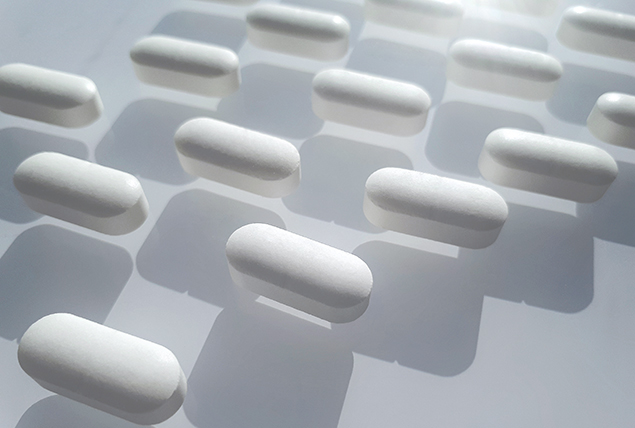 A row of white pills lay in a pattern casting shadows along a white surface.
