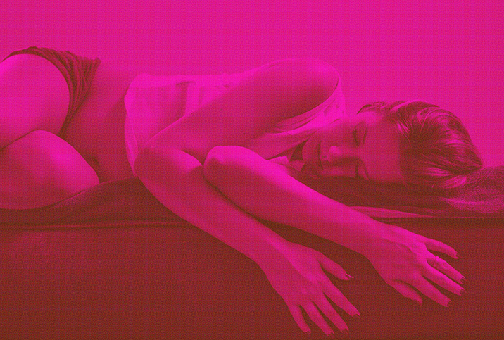 A pink image of a woman laying down in pain
