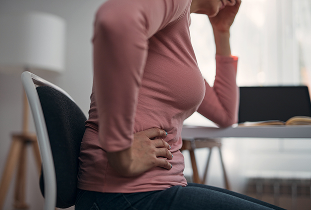 A woman in a pink shirt holds the side of her stomach with one hand and her head with the other.