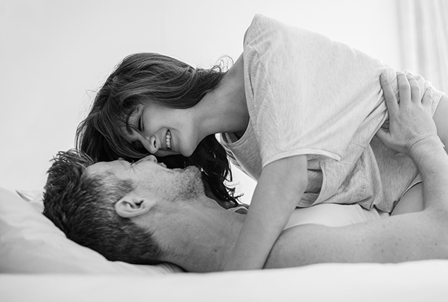 A woman lays over a man as they are about to kiss in bed.