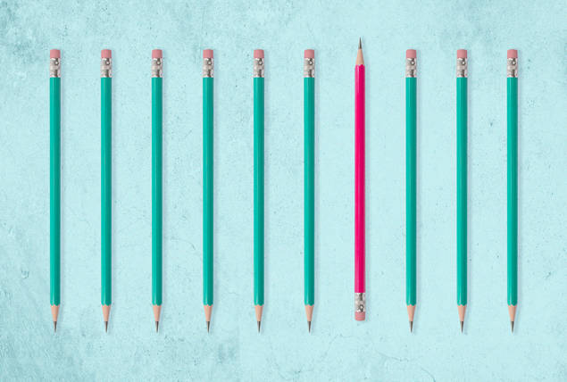 Green pencils are lined up in a row with one pink pencil facing the other direction.
